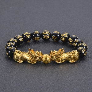 Macro shot of dual golden PiXiu charms and Mani Mantra beads on black obsidian bracelet