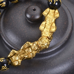 Macro detail of golden Pi Xiu charm with obsidian beads and engraved mantras