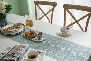 Detailed view of woven teal table runner with white reindeer pattern on a white cloth