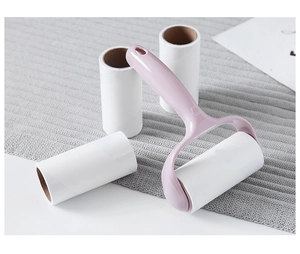 Pink lint roller handle and three white adhesive refill rolls on a grey knitted surface