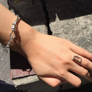 Close-up of a silver knot woven bracelet and a minimalist ring with a clear gemstone
