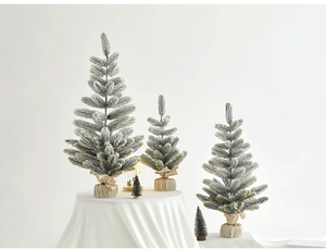 Three flocked mini Christmas trees with burlap bases on a white linen tabletop