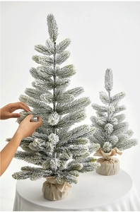 Detail of two mini flocked Christmas trees with snow effect and burlap bases on a pedestal