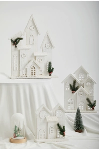 Three white wooden Christmas houses with pine branches and red berries on white fabric
