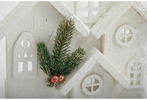 Macro detail of white wooden Christmas house with green pine needles and red berries
