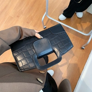 Close-up of black crocodile pattern handbag featuring a unique square handle design