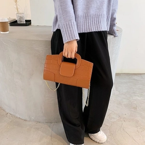 Detailed view of brown crocodile texture handbag with gold chain strap held by a model