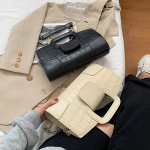 Crocodile pattern handbags in black and beige with gold chains on a cozy bed