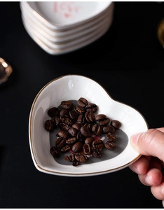 Close-up of heart-shaped white ceramic dish with gold rim holding coffee beans