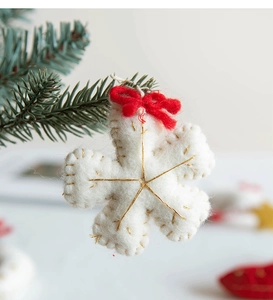 Detail of white felt snowflake ornament with golden stitching and a red bow on tree