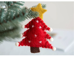 Close-up of handmade red felt Christmas tree ornament hanging on natural pine branch