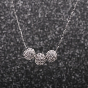 Détail macro d'un collier à trois sphères argentées orné de pavés de zircons cubiques