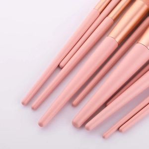 Close-up of pink makeup brush handles with rose gold ferrules on a soft pastel background