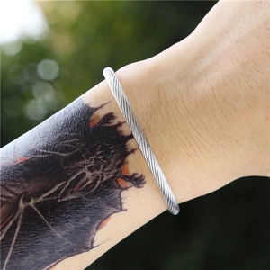 Close-up of a silver twisted steel open cuff bracelet on a tattooed wrist with greenery