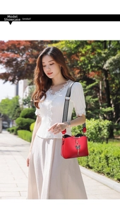 Detail of red crossbody bag with black butterfly charm and patterned strap in park setting