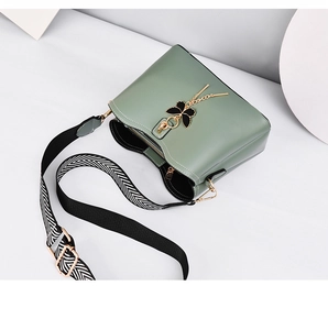 Detail of green bucket bag featuring golden butterfly charm and geometric strap