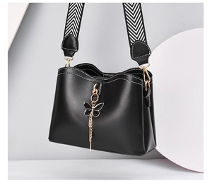 Detail of black bow shell bag with striped wide strap and gold hardware accents