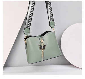 Detail of sage green crossbody shell bag with patterned wide strap and bow charm