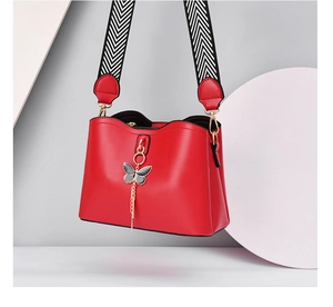 Detail of red shell crossbody bag with bow charm and black white patterned strap