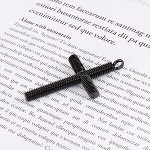 Makroaufnahme eines schwarzen Edelstahl-Kreuzanhängers im Schraubendesign auf Papier
