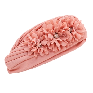 Détail d'un turban plissé rose avec trois fleurs en tissu et centres en perles