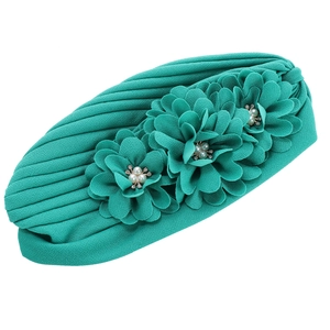Détail du turban plissé turquoise avec trois fleurs en tissu, perles et strass brillants