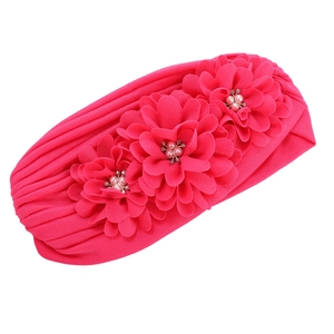 Détail d'un bonnet turban rose vif avec trois fleurs en tissu ornées de perles et strass
