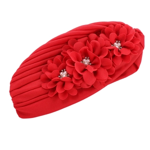 Détail d'un bonnet turban rouge avec trois fleurs en tissu ornées de perles et de strass