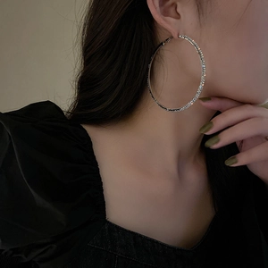 Close-up of model wearing large silver-toned hoop earrings with paved white rhinestones