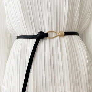 Minimalist black PU leather waist belt with gold horseshoe buckle on a white pleated dress