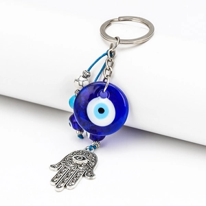 Close-up of blue glass evil eye and metal Hamsa hand pendant on a silver keychain