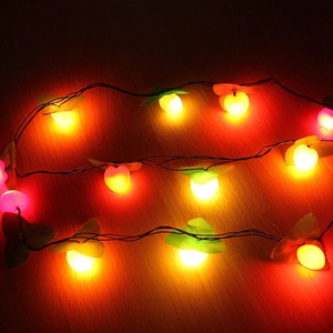 LED apple-shaped Christmas lights with red and yellow spheres and green leaves on wood