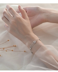 Detail of silver double-layer bracelet with letter D pendant on a soft floral background