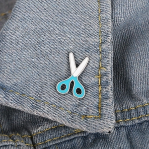 Detail of blue and white enamel scissor brooch pinned on denim fabric lapel
