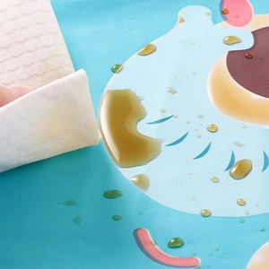 Waterproof blue cartoon silicone baby bib being wiped clean with a paper towel