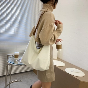 Detailed view of cream white tote bag worn by a model in a minimalist indoor setting