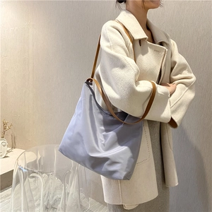 Close-up of a large purple canvas tote bag with brown leather straps worn by a model