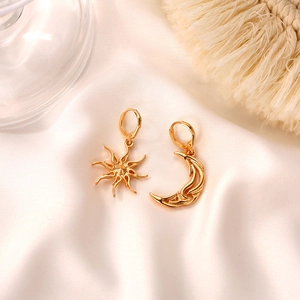 Macro detail of asymmetric gold sun and moon earrings on white silk background