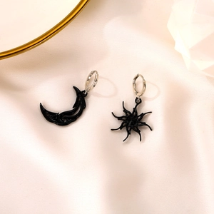 Asymmetric sun and moon black charm earrings on minimalist cream silk fabric background