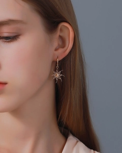 Close-up of a gold sun-shaped earring worn by a model on a clean blue-grey background