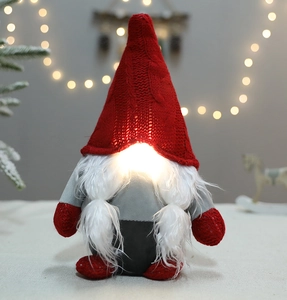Illuminated Christmas gnome plush with red knit hat and warm LED glow on snowy backdrop