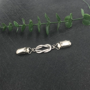 Detailed view of a silver knot-shaped metal cardigan clip for sweaters and shawls