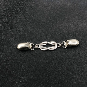 Silver vintage knot cardigan clip with duckbill clamps on a dark textured background