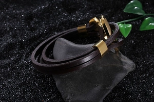 Detailed shot of brown braided leather bracelet with golden anchor clasp on stone background