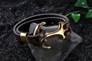 Close-up of golden anchor clasp on braided dark brown leather bracelet over dark rock