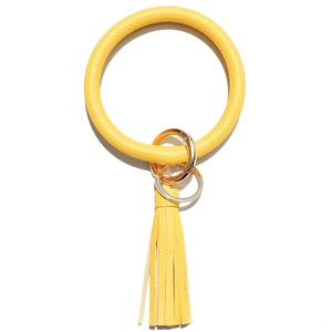 Detailed view of yellow faux leather keyring bangle with tassel and gold metal hardware