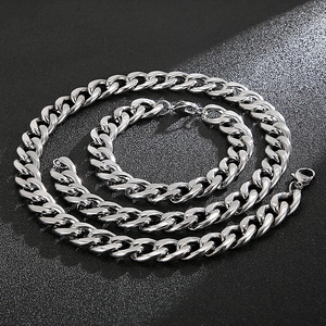 Macro detail of polished silver Cuban link chain necklace and bracelet set on black stone