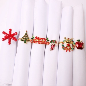 Detail showing five varied Christmas napkin rings with enamel and rhinestones on white linens