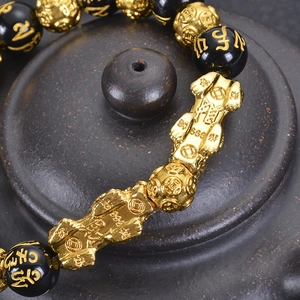 Golden Pixiu bracelet with black beads and Six-Word Mantra engraving on dark ceramic