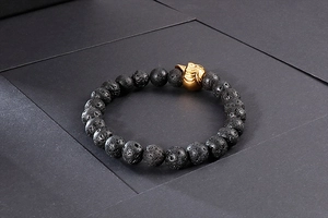 Gros plan de perles de lave noires mates et breloque tête de mort dorée sur bracelet élastique